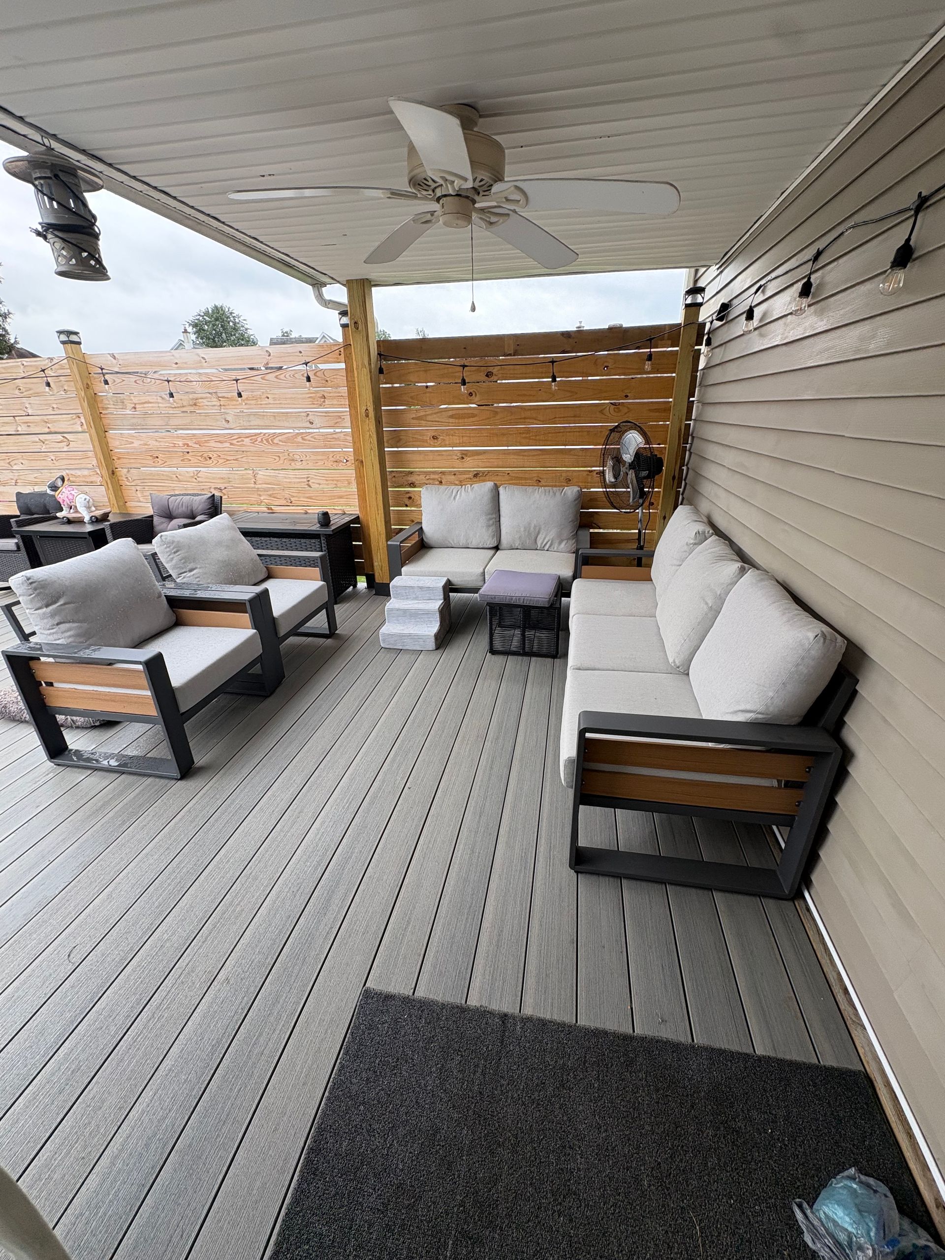 Deck with gray outdoor seating, wooden privacy walls, and a ceiling fan.