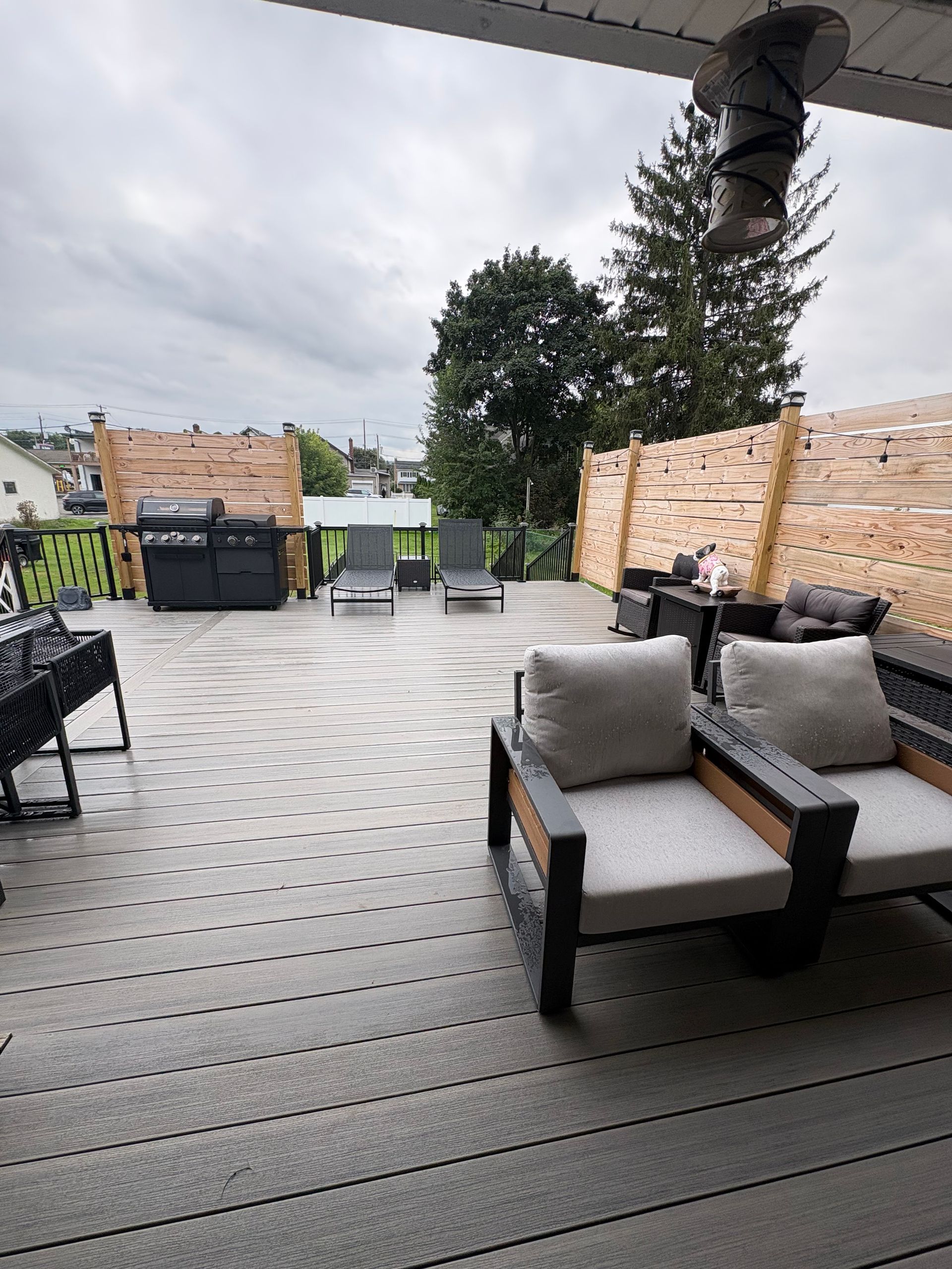Deck with wicker chairs, gray cushions, and a tiled floor under a covered roof, overlooking an outdoor view