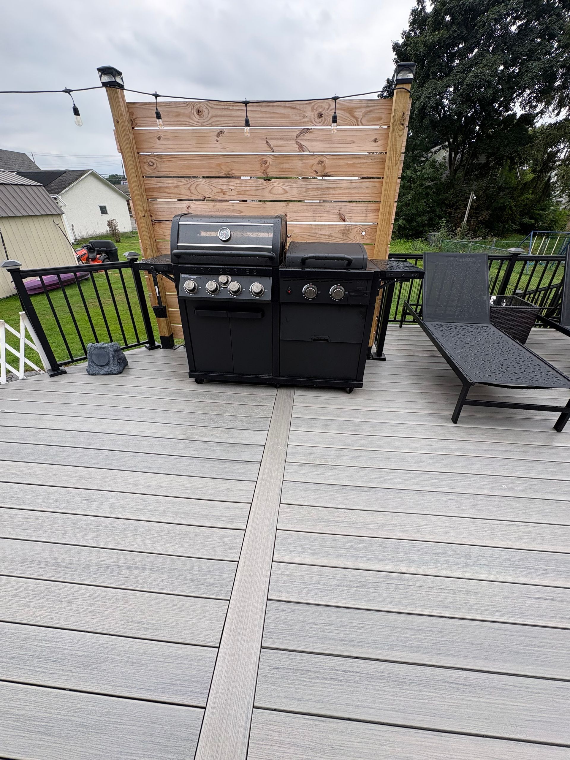 Deck with a black gas grill and wooden privacy screen between outdoor chairs and a gray deck