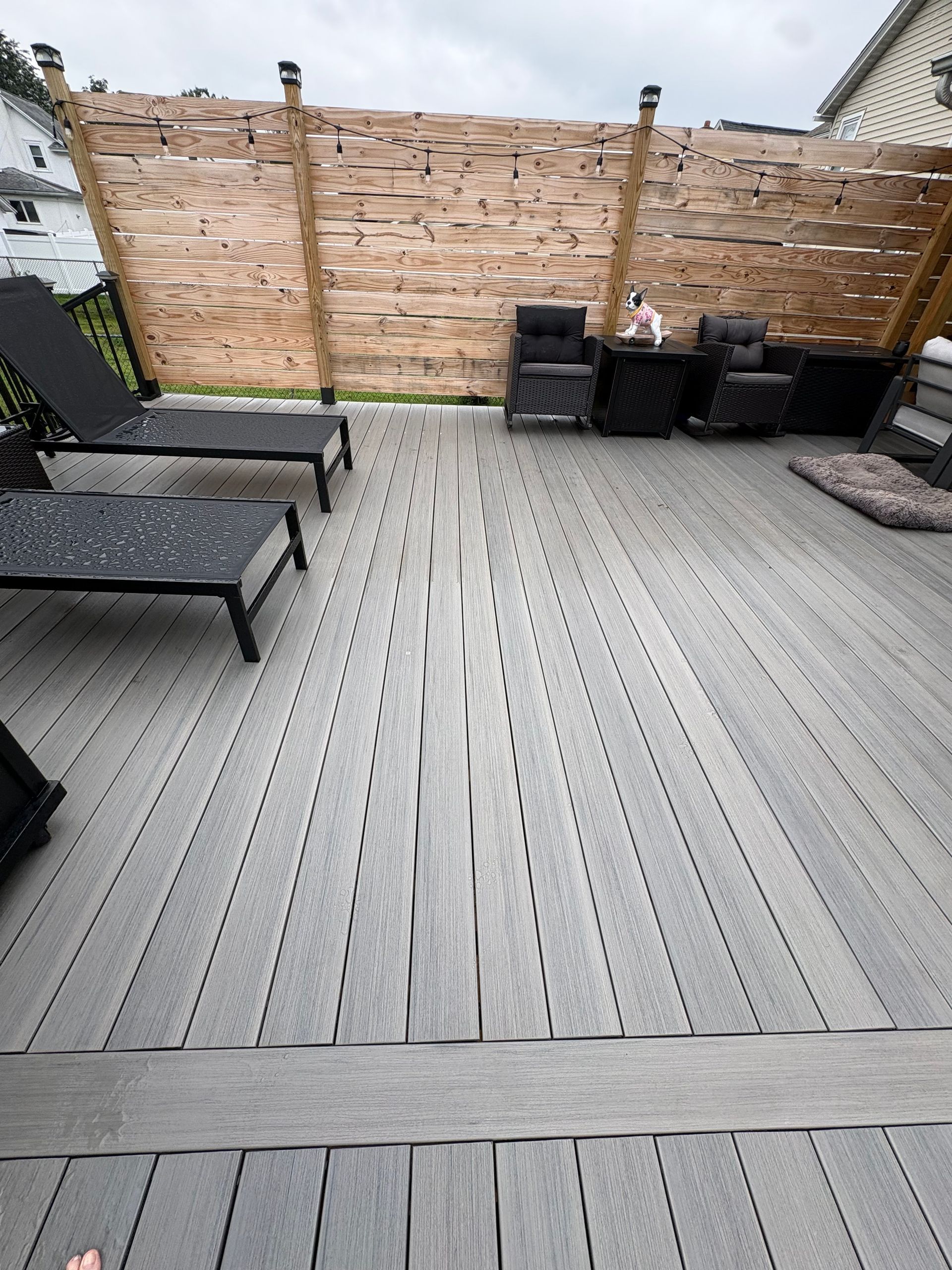 Deck with outdoor lounge chairs, black storage boxes, and a wooden privacy fence.