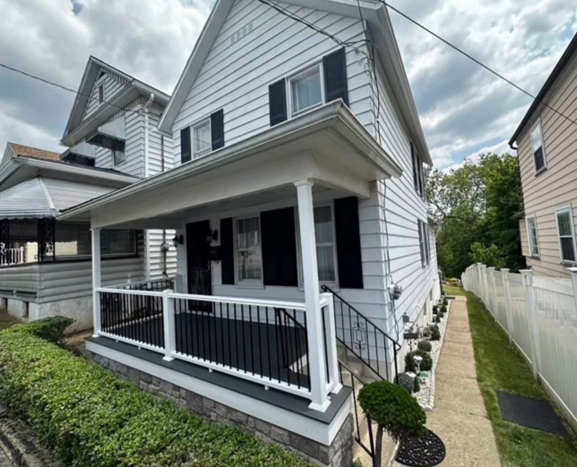 White two-story house with a covered porch and narrow side walkway, seen from the street