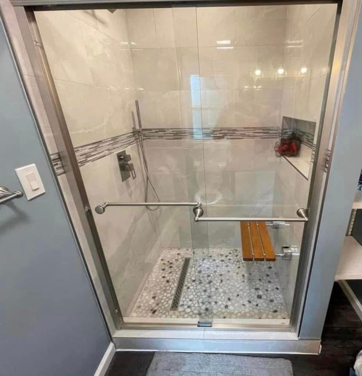 Walk-in glass shower with white tile walls, pebble floor, built-in shelf, and chrome grab bar.