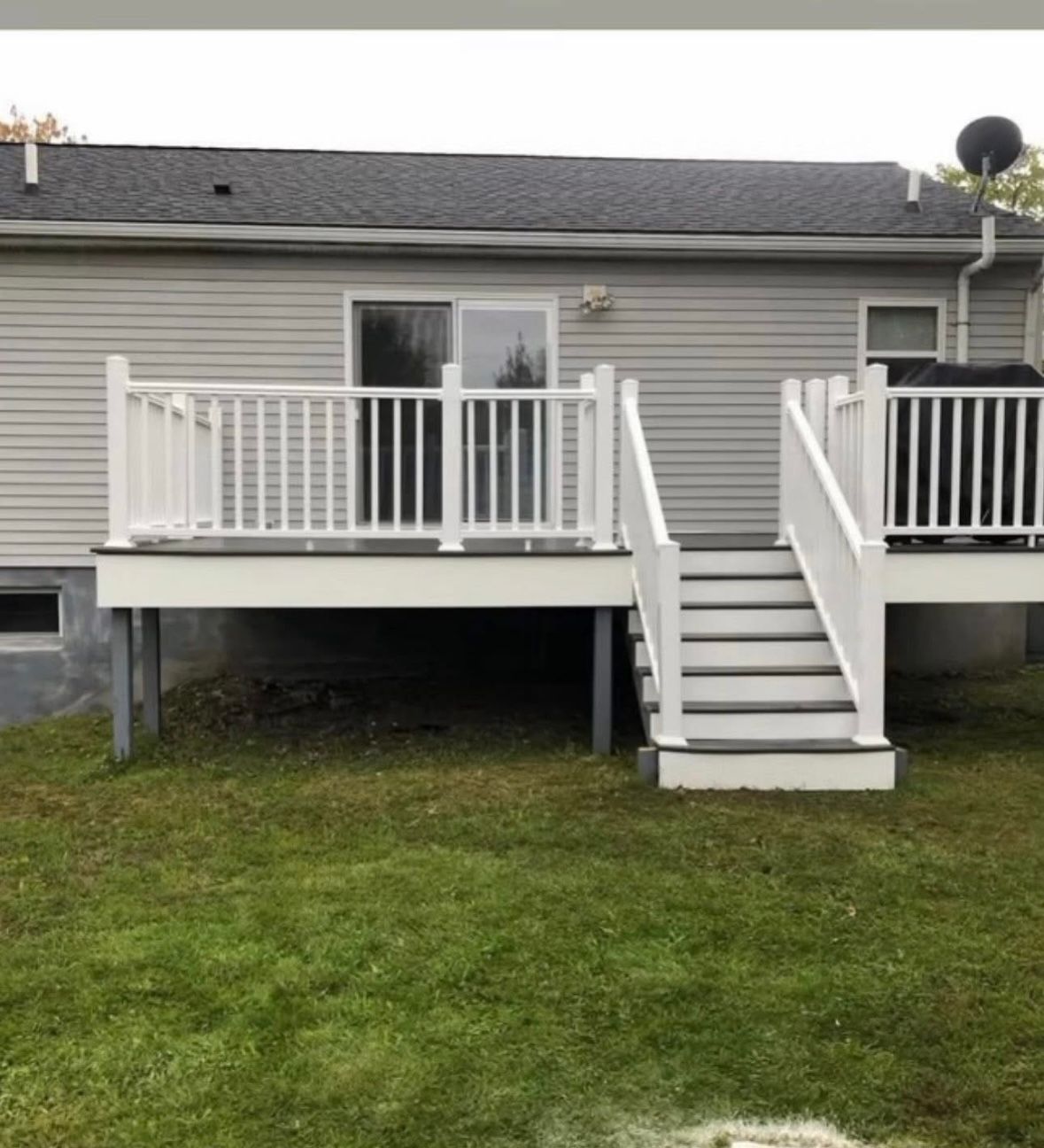 Back deck with white railings and central stairs on the back of a gray house, above a grassy yard