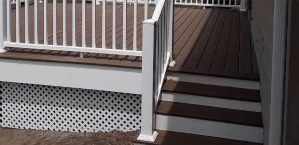 Covered porch with white railings and brown steps leading to a dark wooden deck.