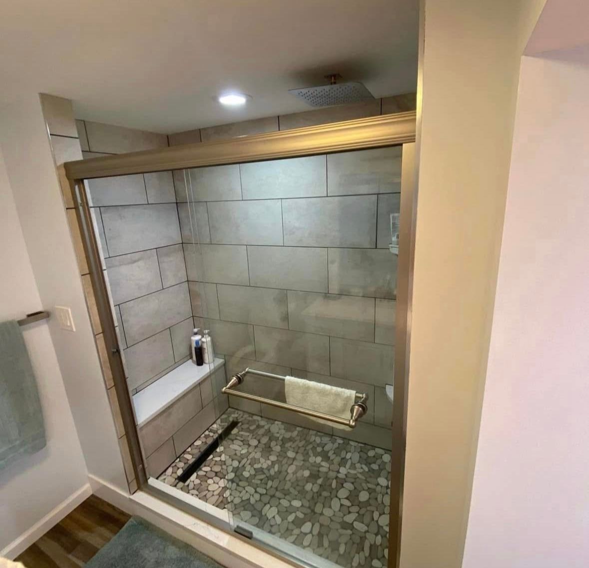 Bathroom shower with gray tile, glass opening, and pebble floor, viewed from the doorway