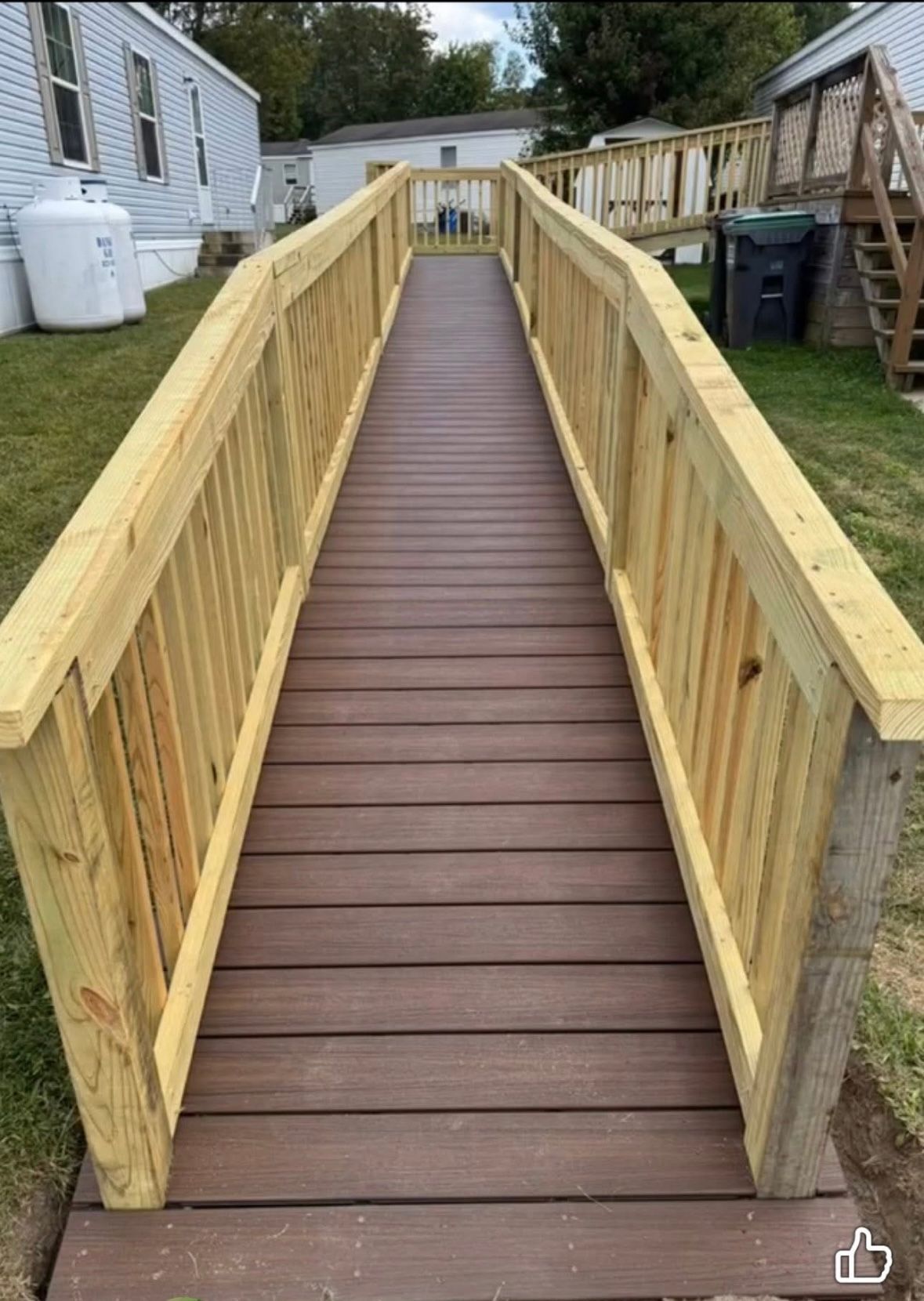 Wooden accessibility ramp with railings leading between mobile homes in a yard