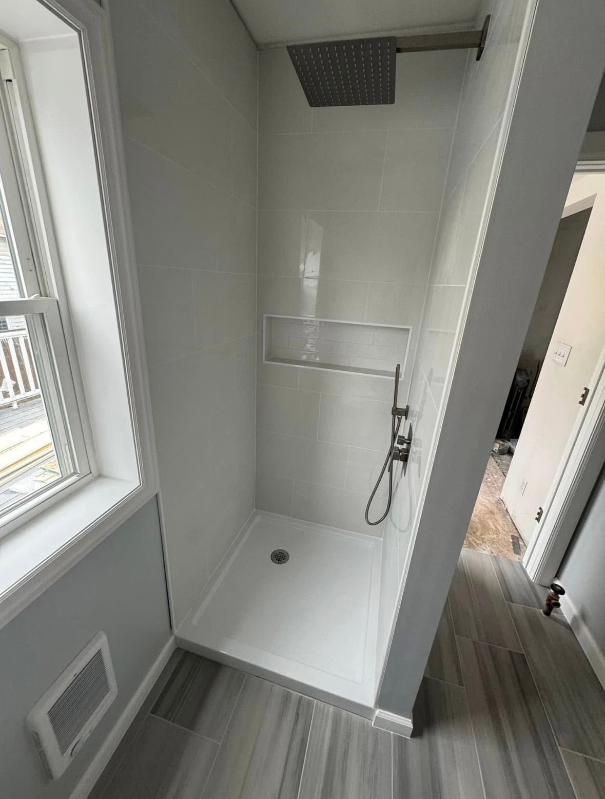 Small tiled shower stall with handheld showerhead, drain, and window light.