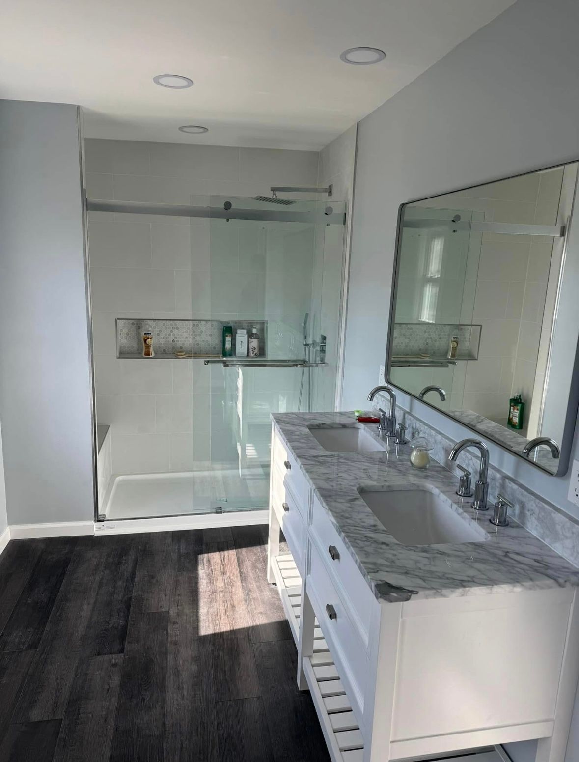 Modern bathroom with glass shower, double vanity, and large wall mirror in gray and white tones