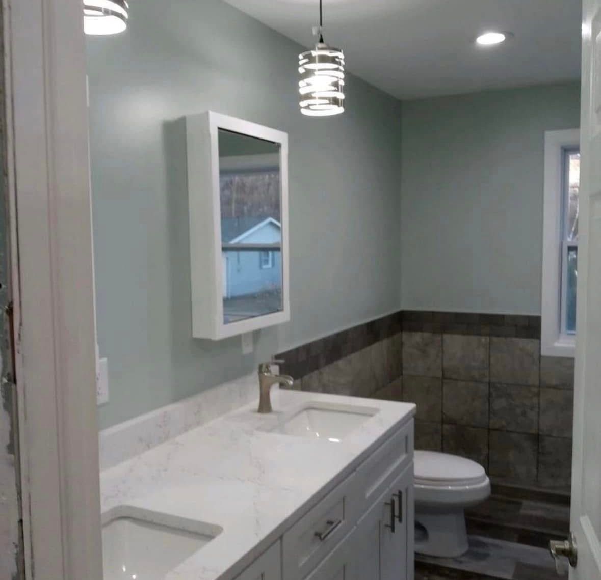 Modern bathroom with white vanity, gray walls, tiled shower surround, and a hanging light fixture