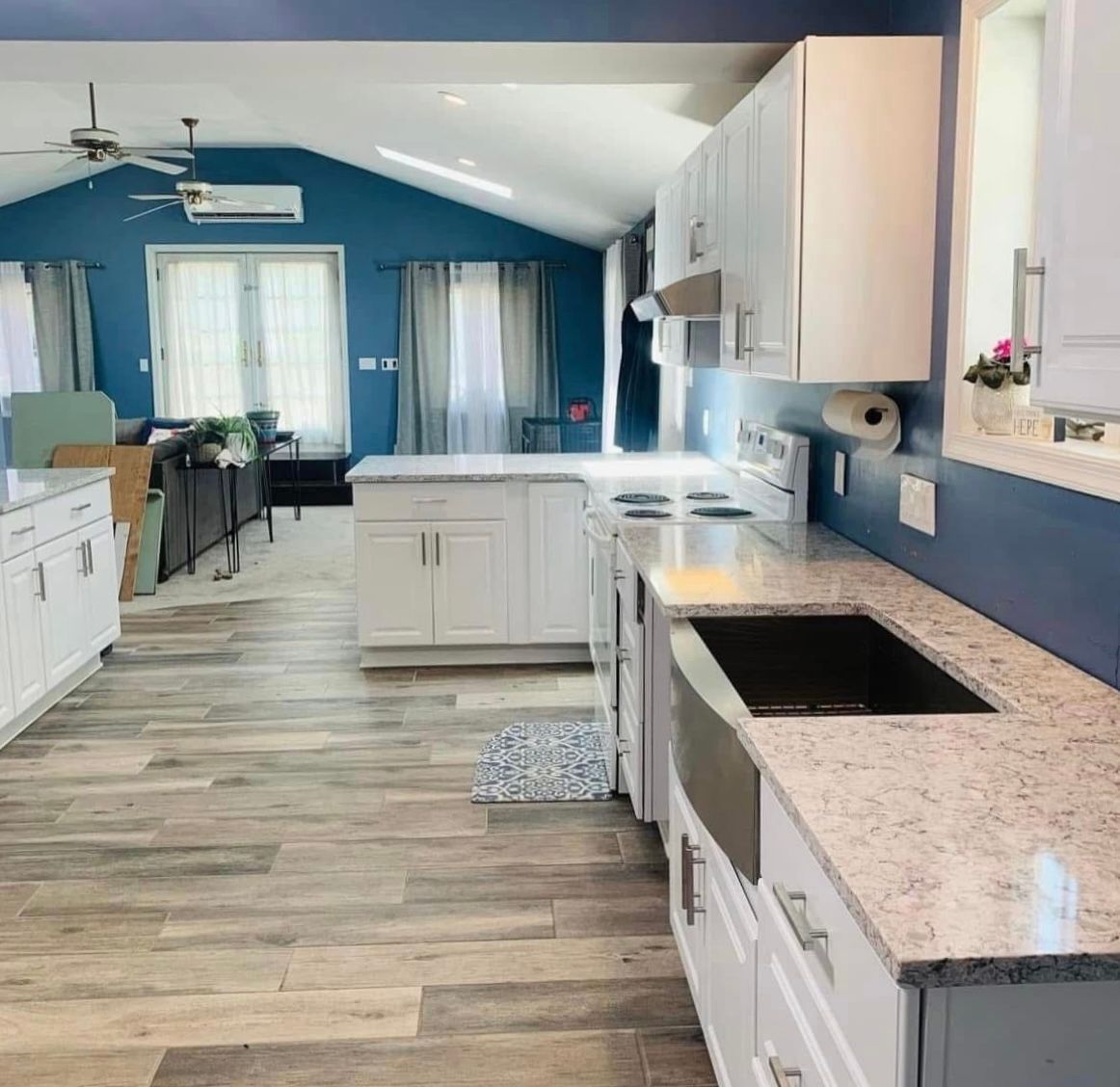 Bright kitchen with blue walls, white cabinets, and wood floors, viewed from the island.