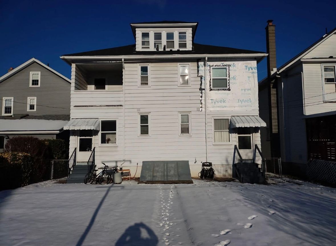Snow-covered white house with front steps and neighboring homes on either side