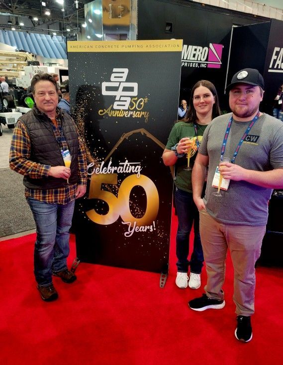 Three people are standing in front of a 50th anniversary sign.