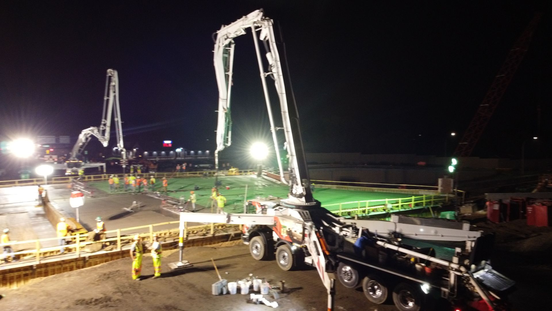 A concrete pump is being used to pump concrete into a pool at night.