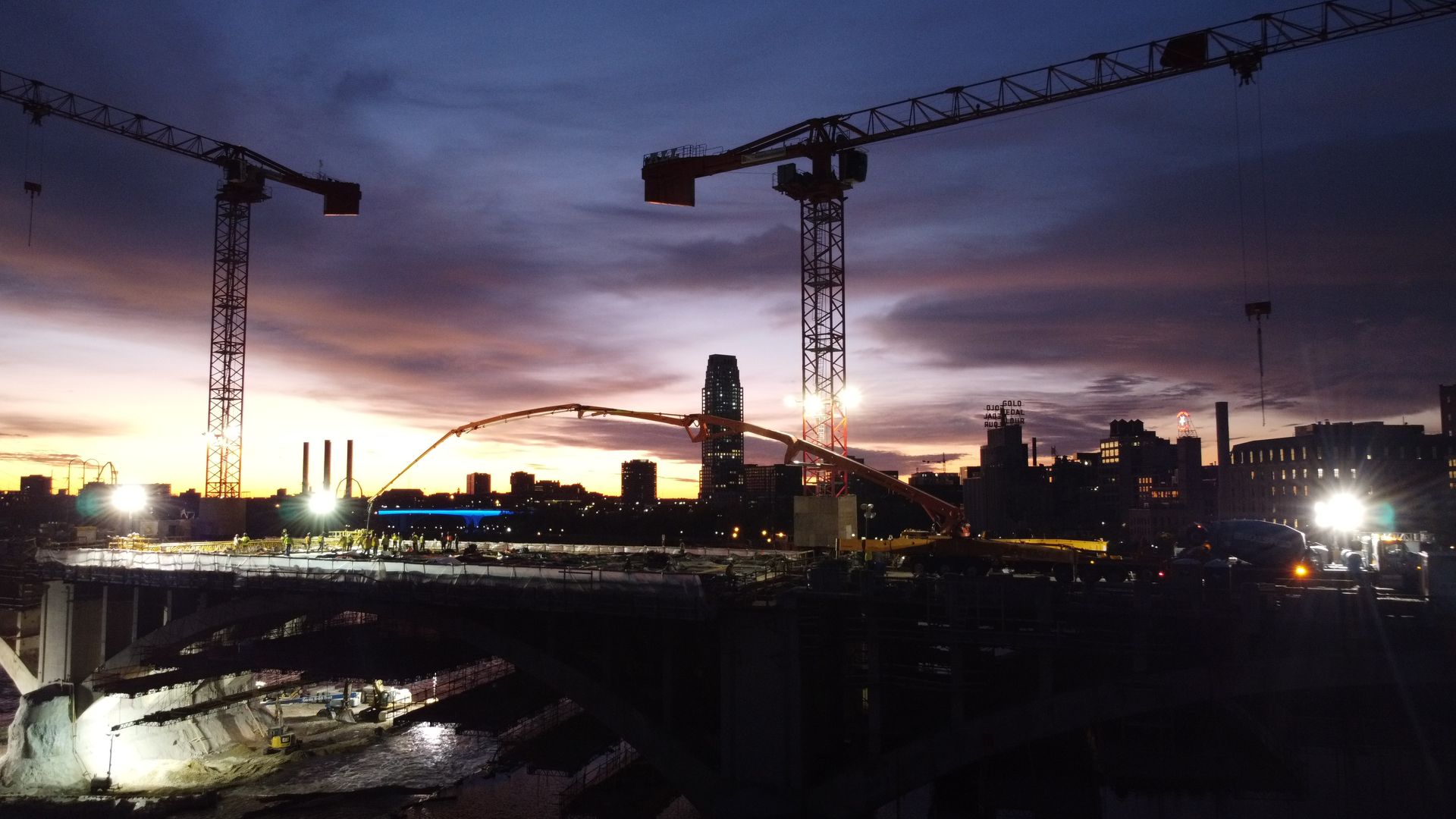 A construction site at night with cranes and a sunset in the background