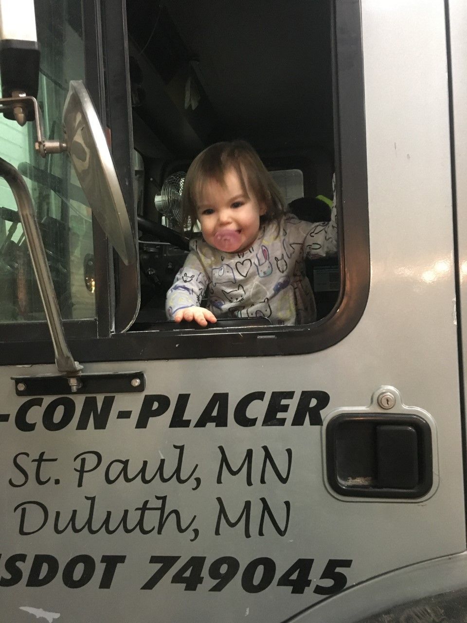 A little girl is sitting in the driver 's seat of a con-placer truck