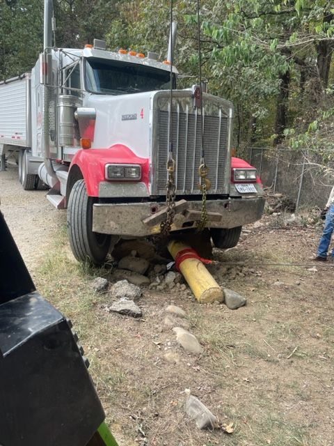 Semi-truck with a red and white cab stuck on a dirt road, supported by a wooden log.