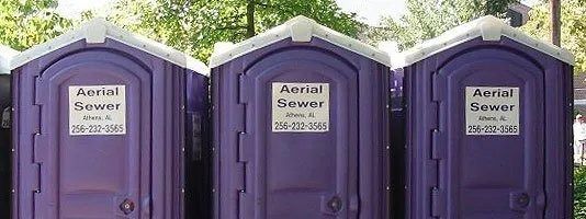 Three purple portable toilets with white roofs lined up outdoors.
