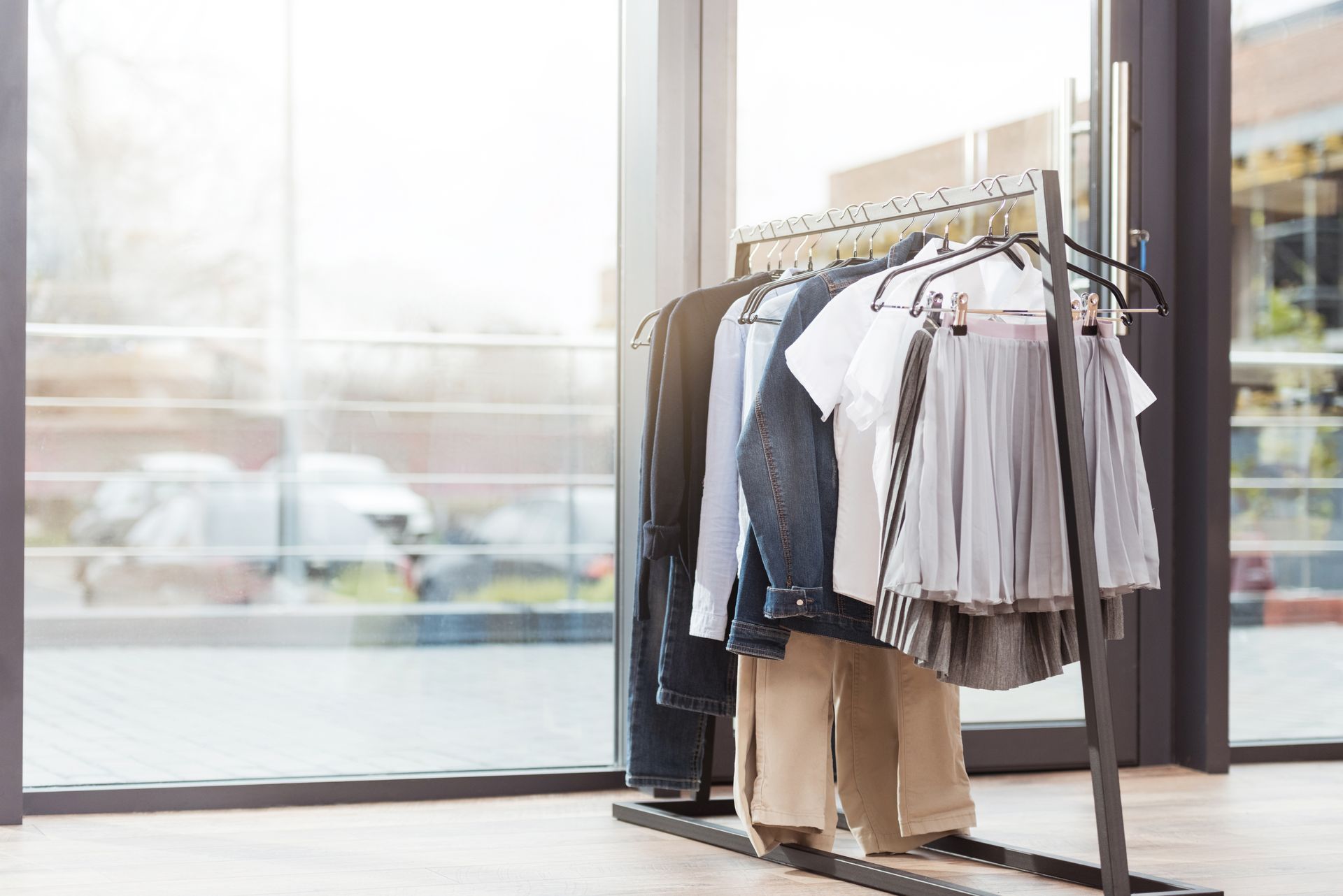 Clothing rack with garments in a bright store window. Neutral colors of clothing on black rack.