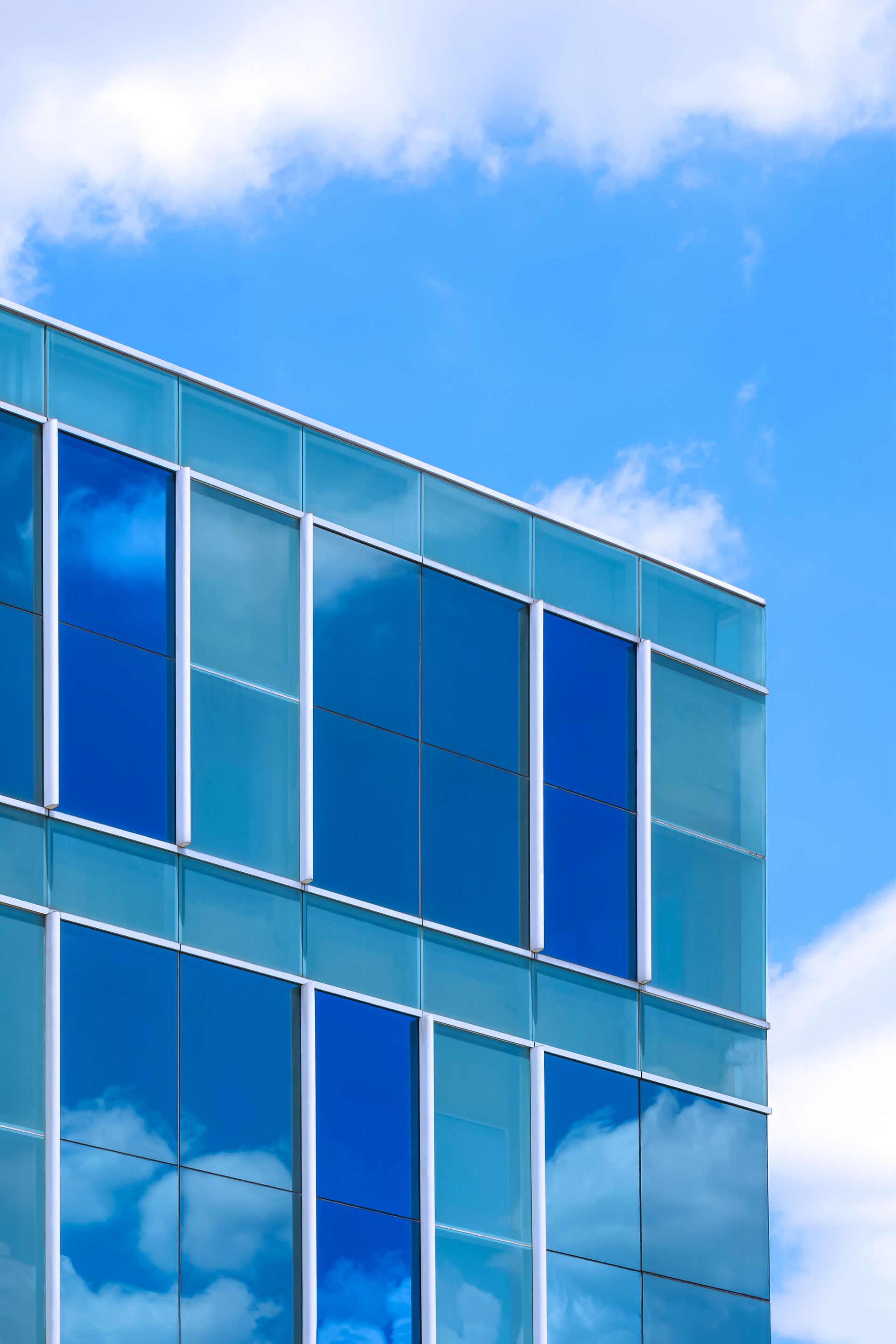Modern building with blue glass windows reflecting a bright blue sky with white clouds.