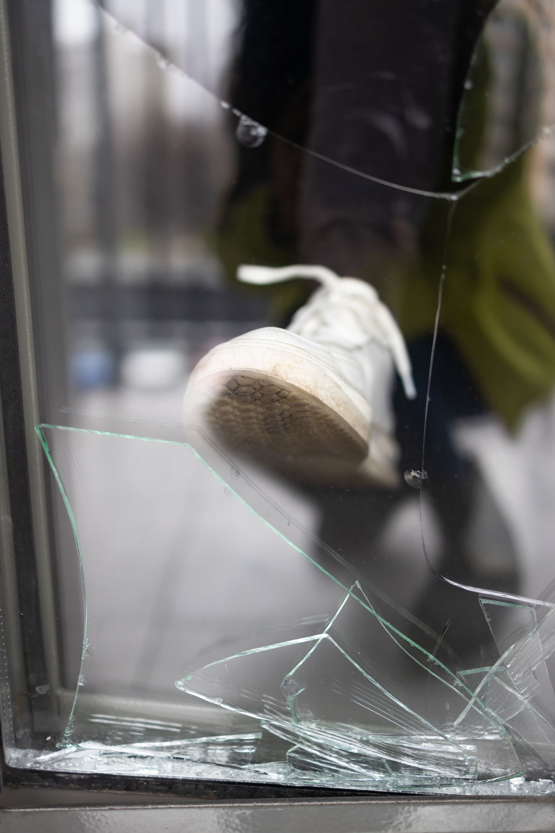 Foot kicking through a cracked glass window, showing a white shoe.