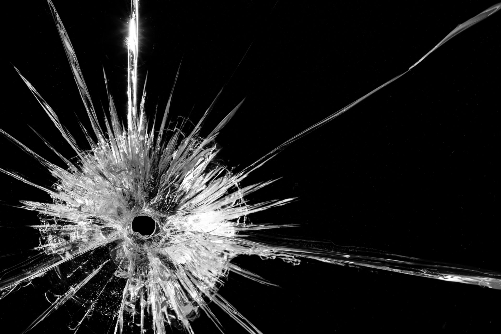 Cracked glass with a central hole, radiating shards against a black background.