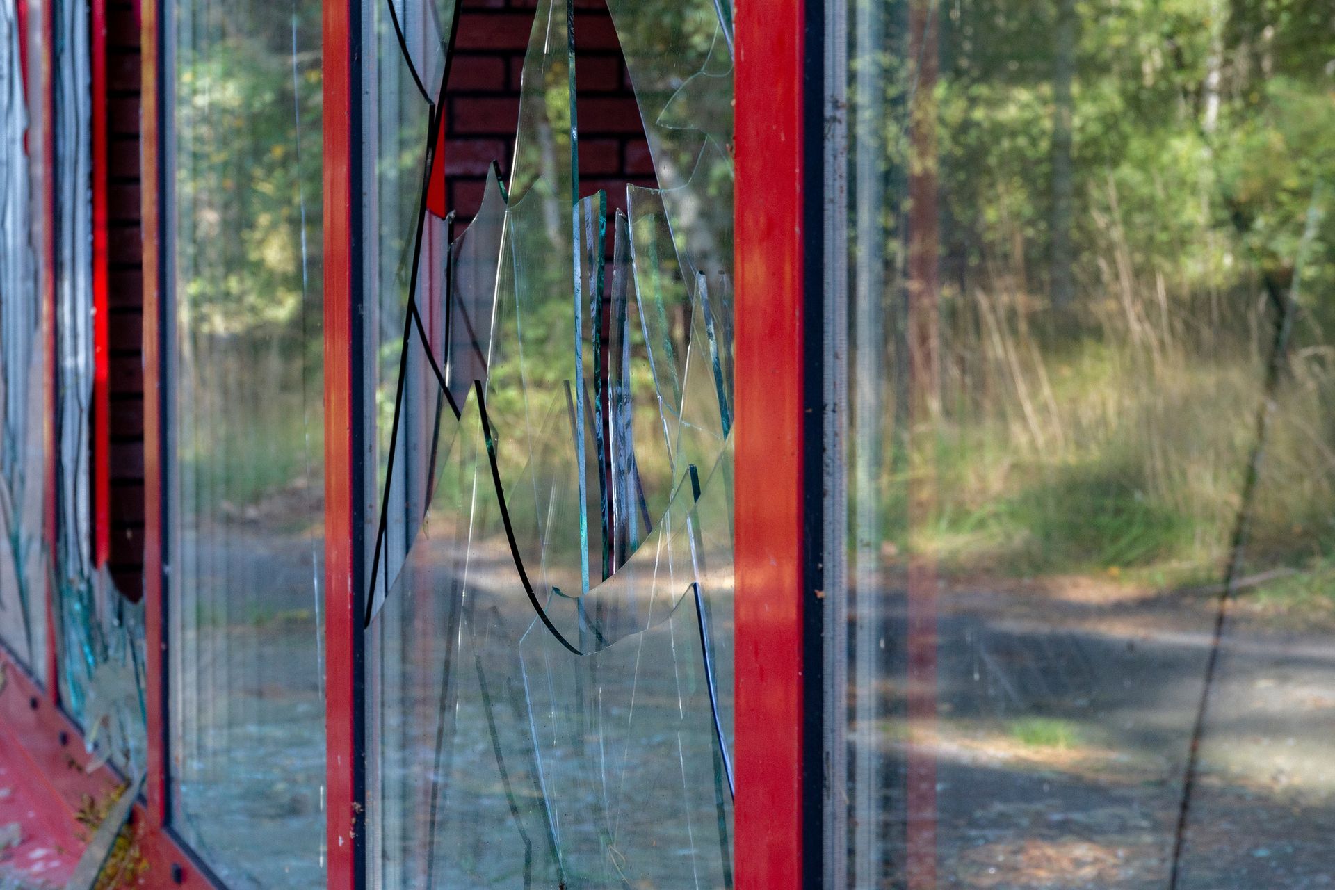 Broken, red-framed phone booth with cracked glass, trees in the background.