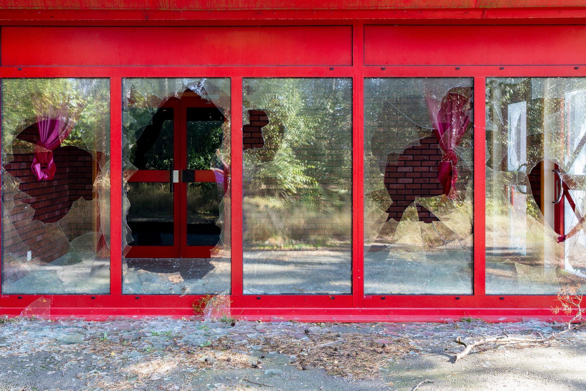 Red-framed building with shattered windows; interior brick visible; debris on ground.
