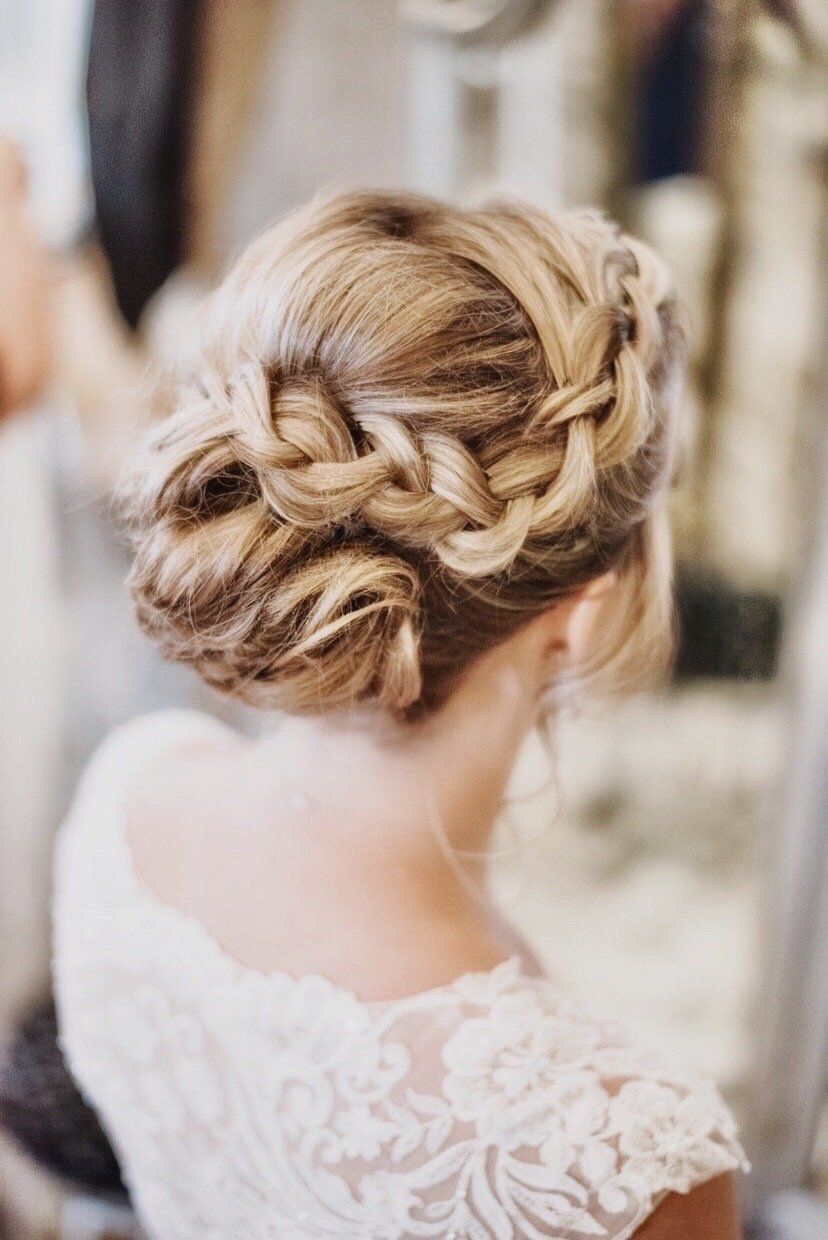 Woman with blonde hair in a braided updo hairstyle, wearing a white lace dress.