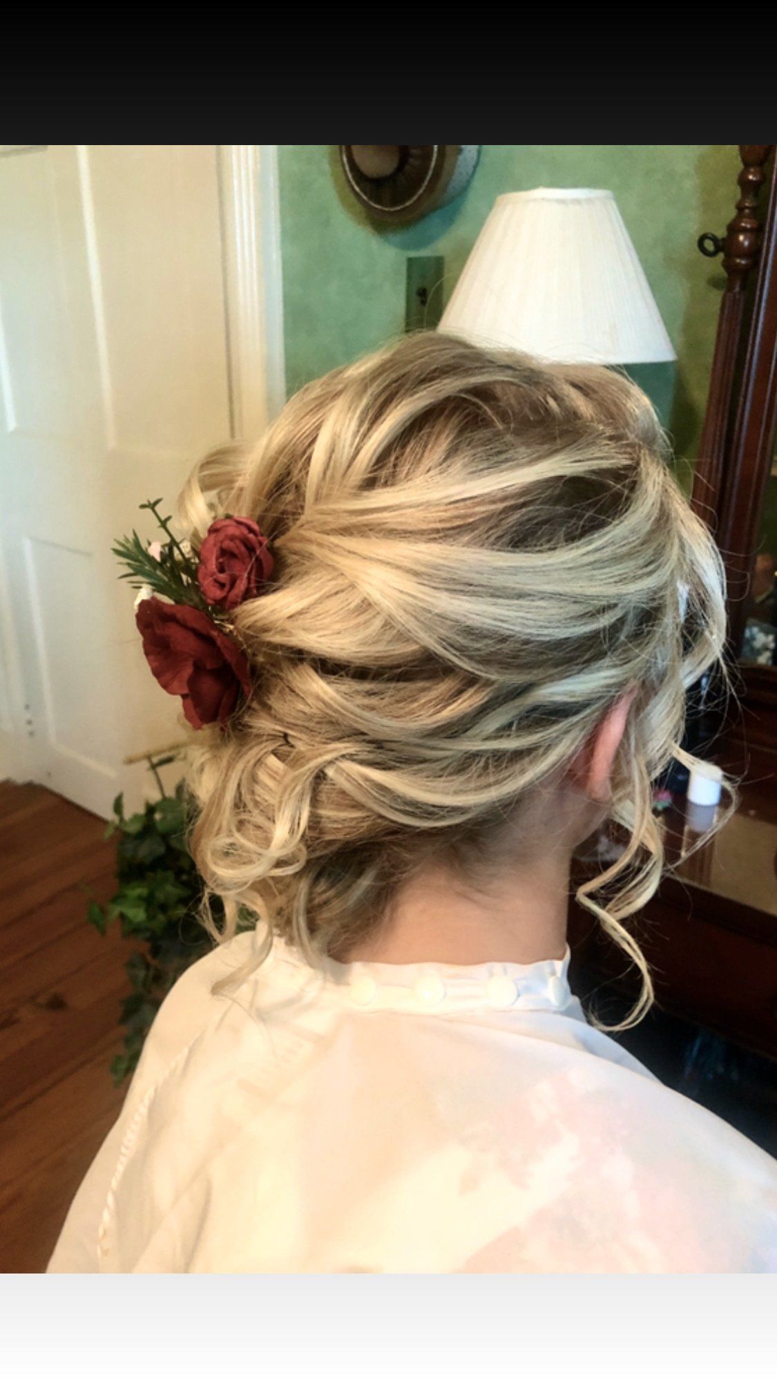Woman with blonde updo hairstyle decorated with burgundy flowers.