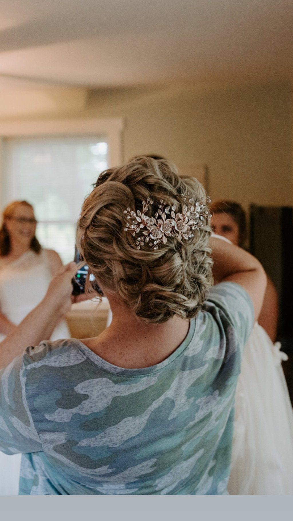 Woman in camo shirt photographs bride with ornate updo and headpiece.