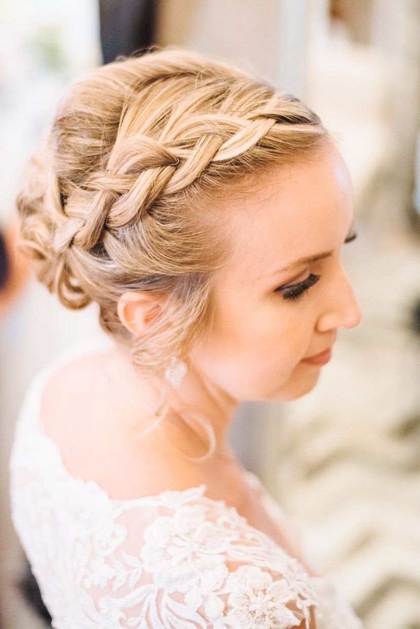 Blonde woman with braided updo hairstyle wearing a white lace dress.
