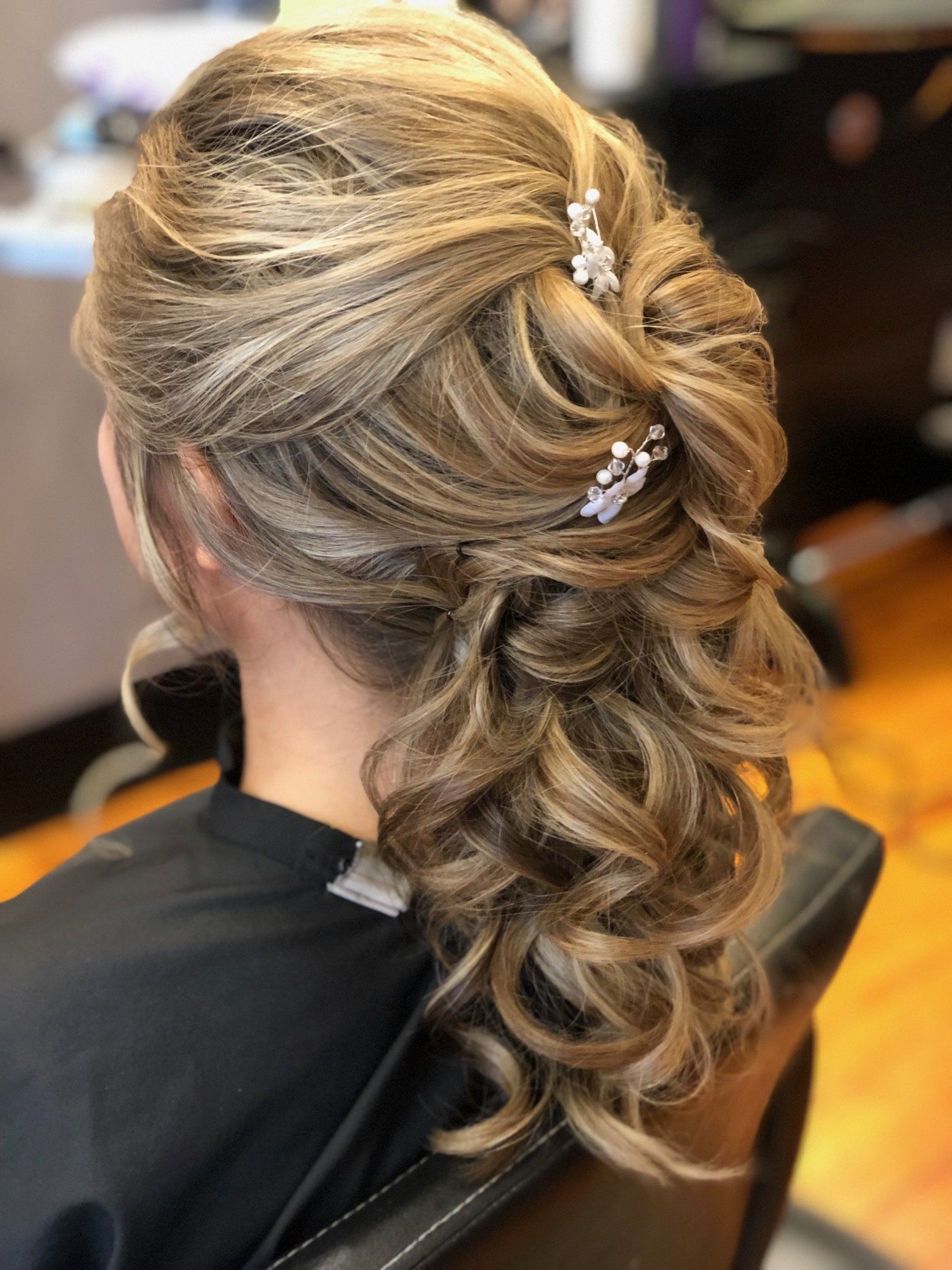 Woman with blonde and brown curled updo hairstyle, styled with hair accessories.