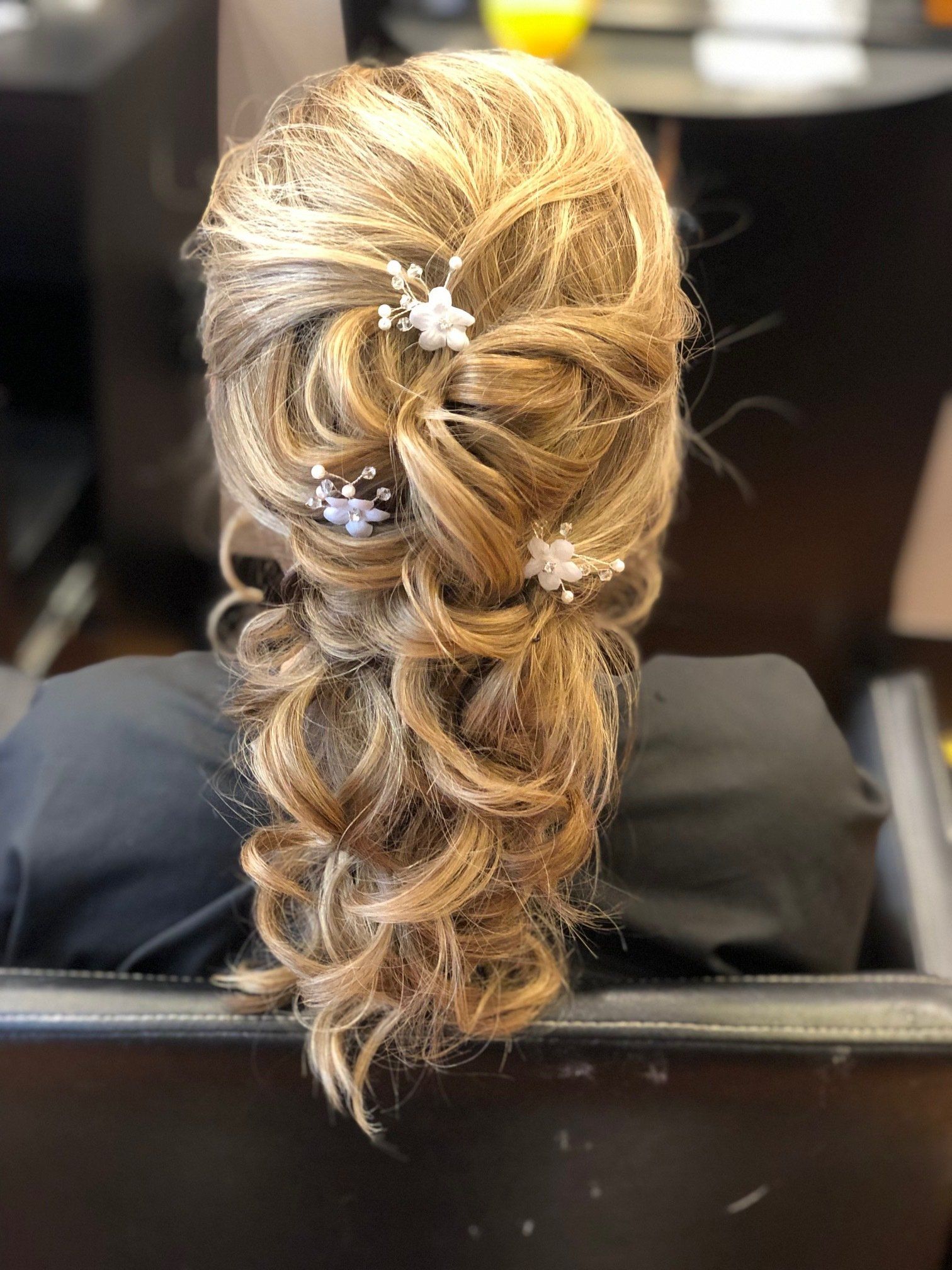 Woman with blonde hair styled in an elegant side braid adorned with small white floral hairpins.