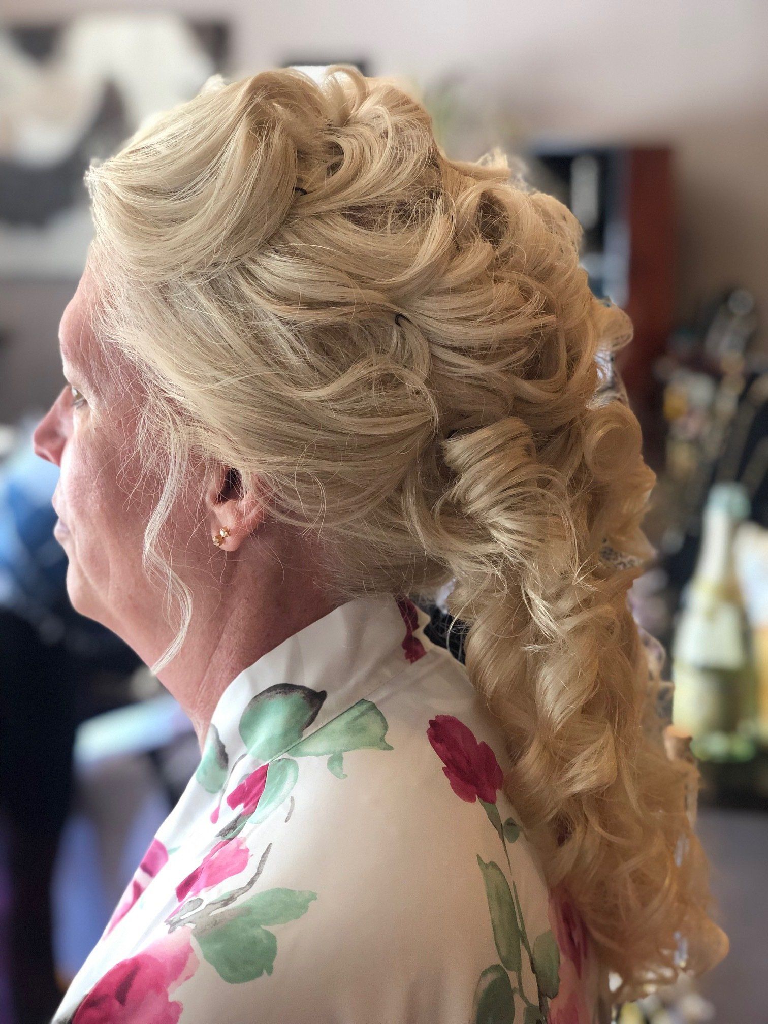 Blonde woman with curly hair styled in an updo, wearing a floral robe.