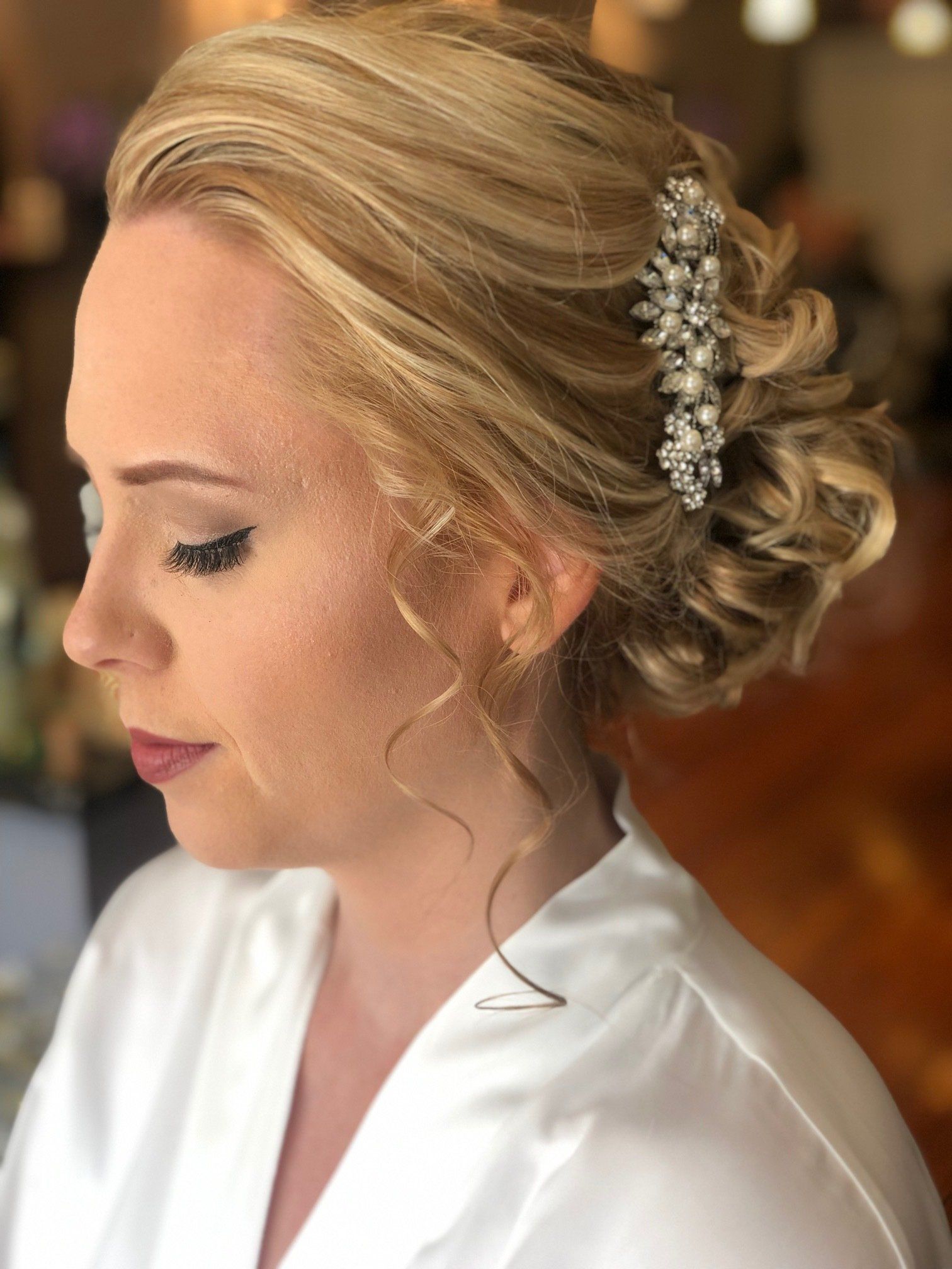 Blonde woman with updo hairstyle and makeup, wearing a white robe, hair accessory.