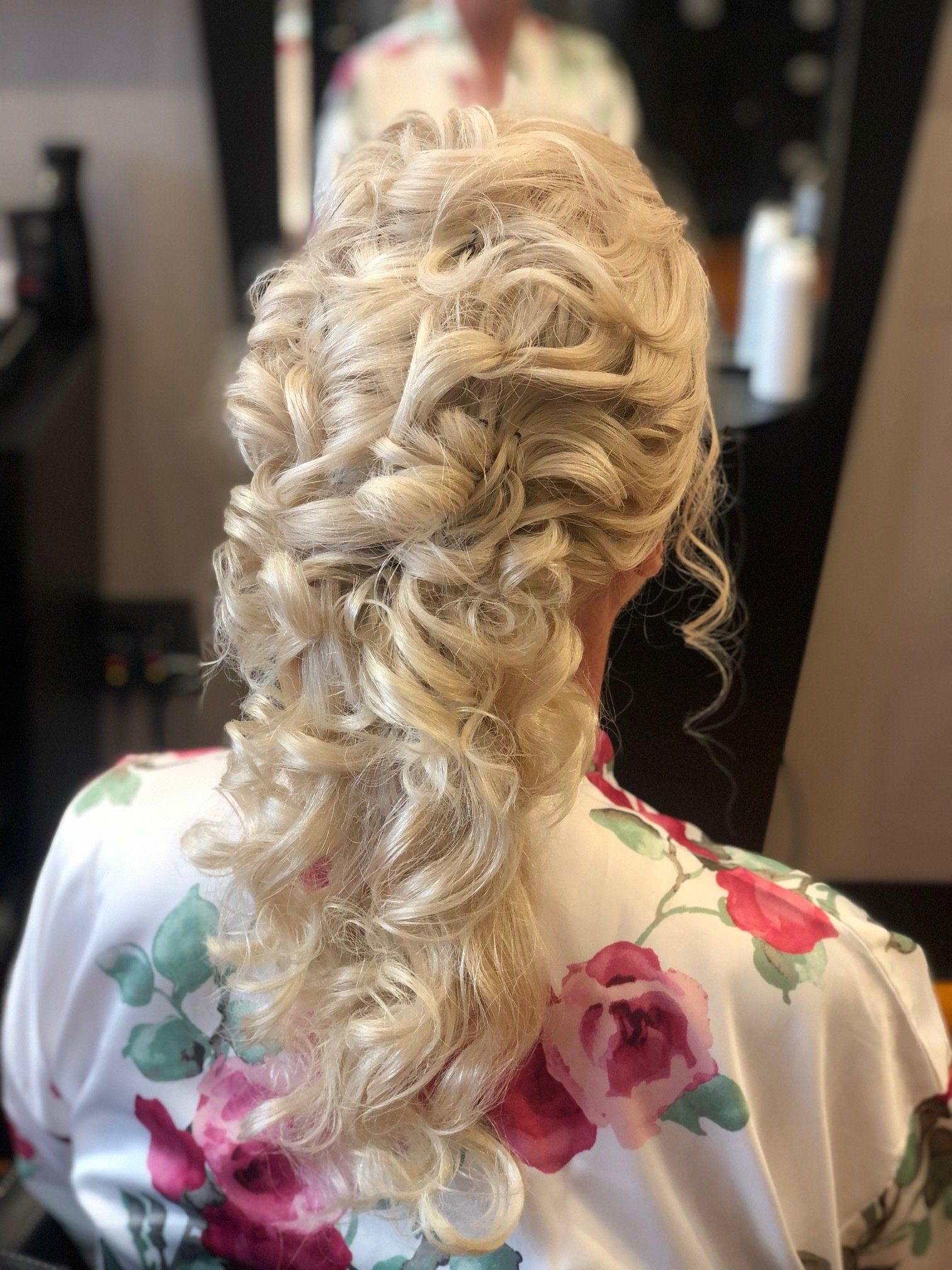 Blonde curly updo hairstyle, viewed from behind. Woman in floral robe, at a salon.