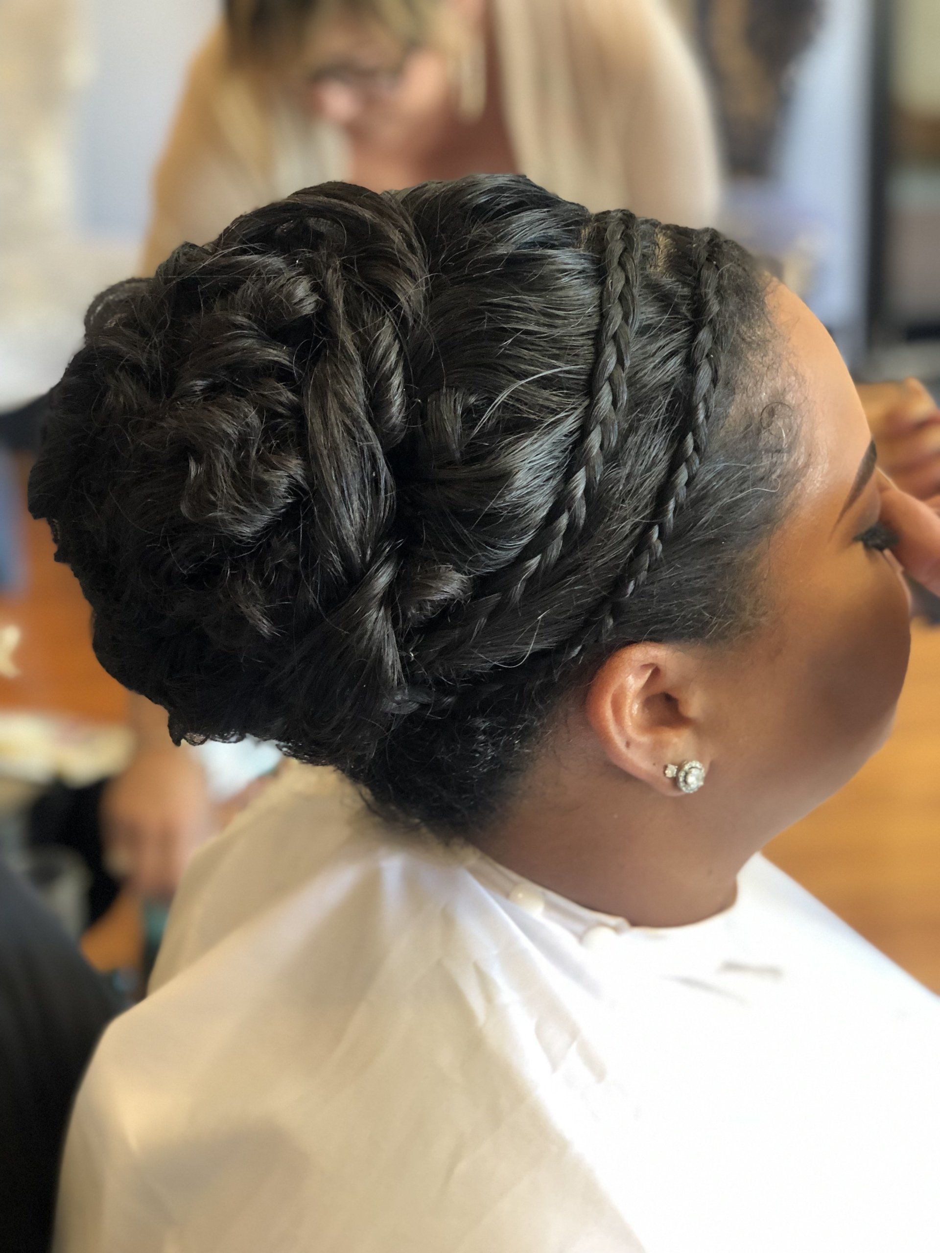 Woman with braided updo hairstyle, wearing earrings, in a salon.