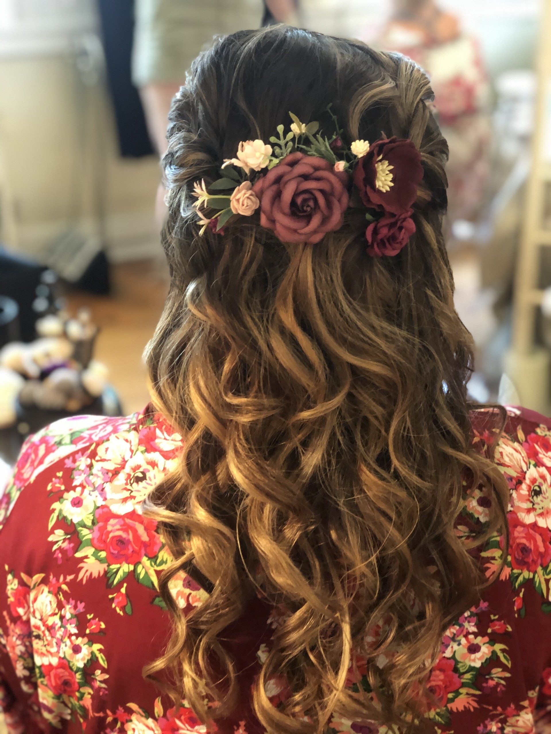 Woman with wavy hair adorned with floral hairpiece, wearing a floral robe.