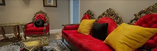 Red sofa and chair with gold ornate trim, yellow and black pillows.