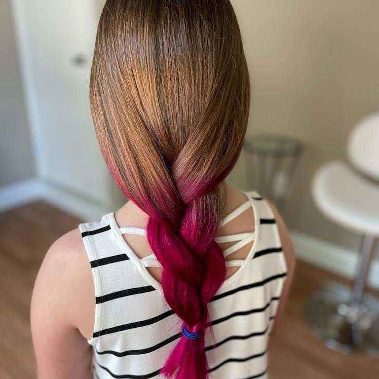 Girl with brown hair braided, transitioning to bright pink. She wears a striped tank top, indoors.