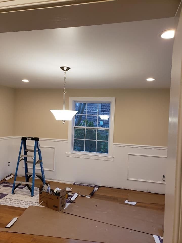 Dining room renovation: Beige walls, white trim, ladder, and a hanging light fixture. Window with outdoor view.