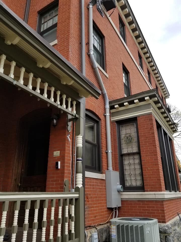 Red brick building exterior with porch, windows, downspout, and AC unit.