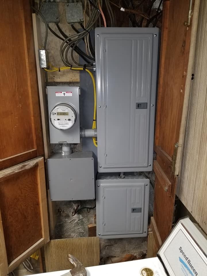 Electrical meter and two breaker boxes mounted in a wooden cabinet. Wires are visible.
