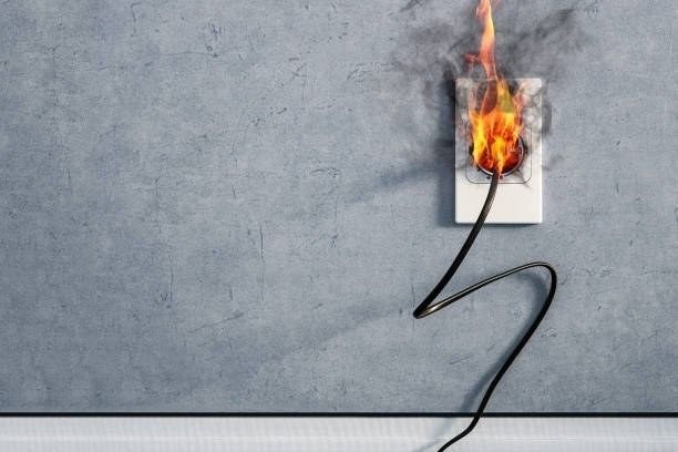 Burning electrical outlet and cord on gray wall. Flames, smoke.