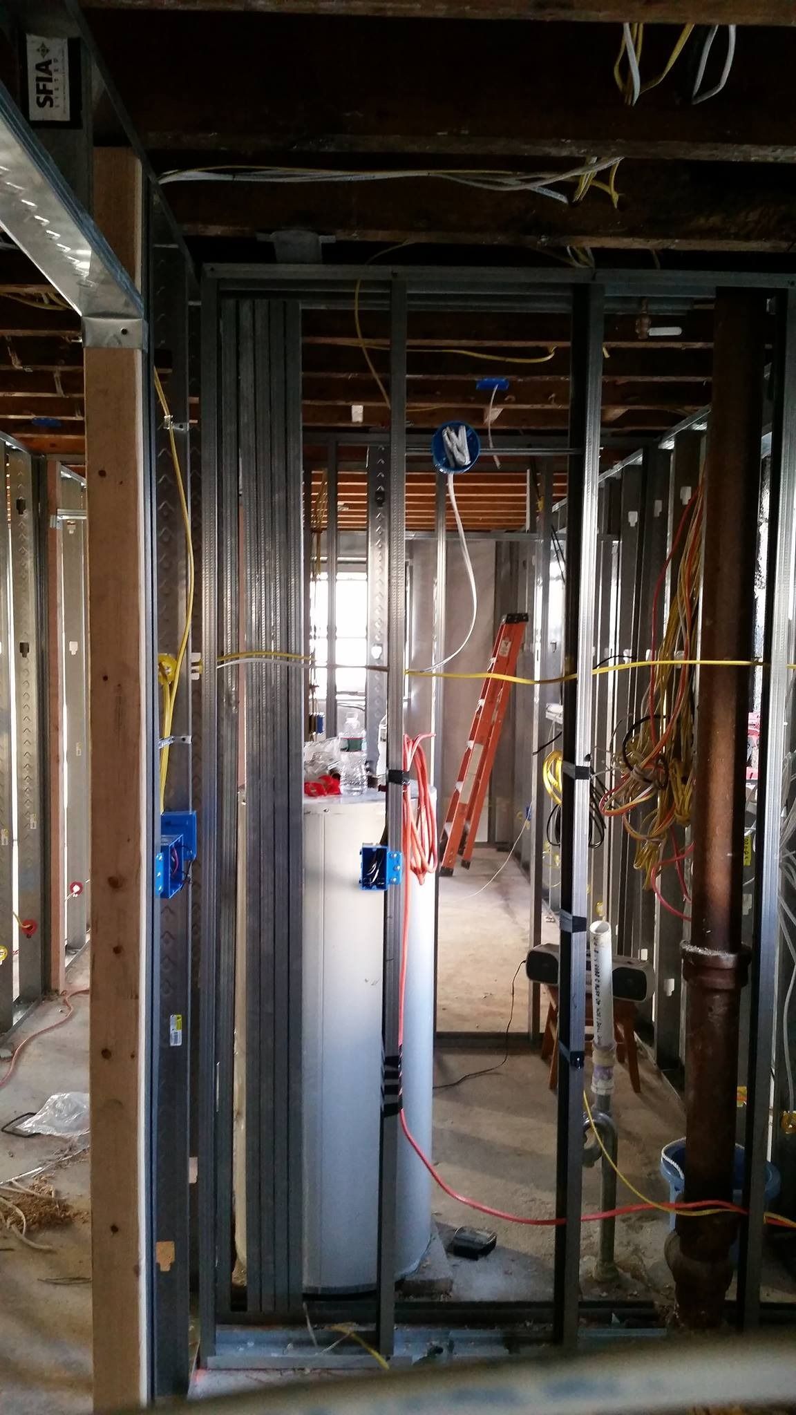 Interior view of a building under construction. Studs, electrical boxes, and plumbing surround a water heater.