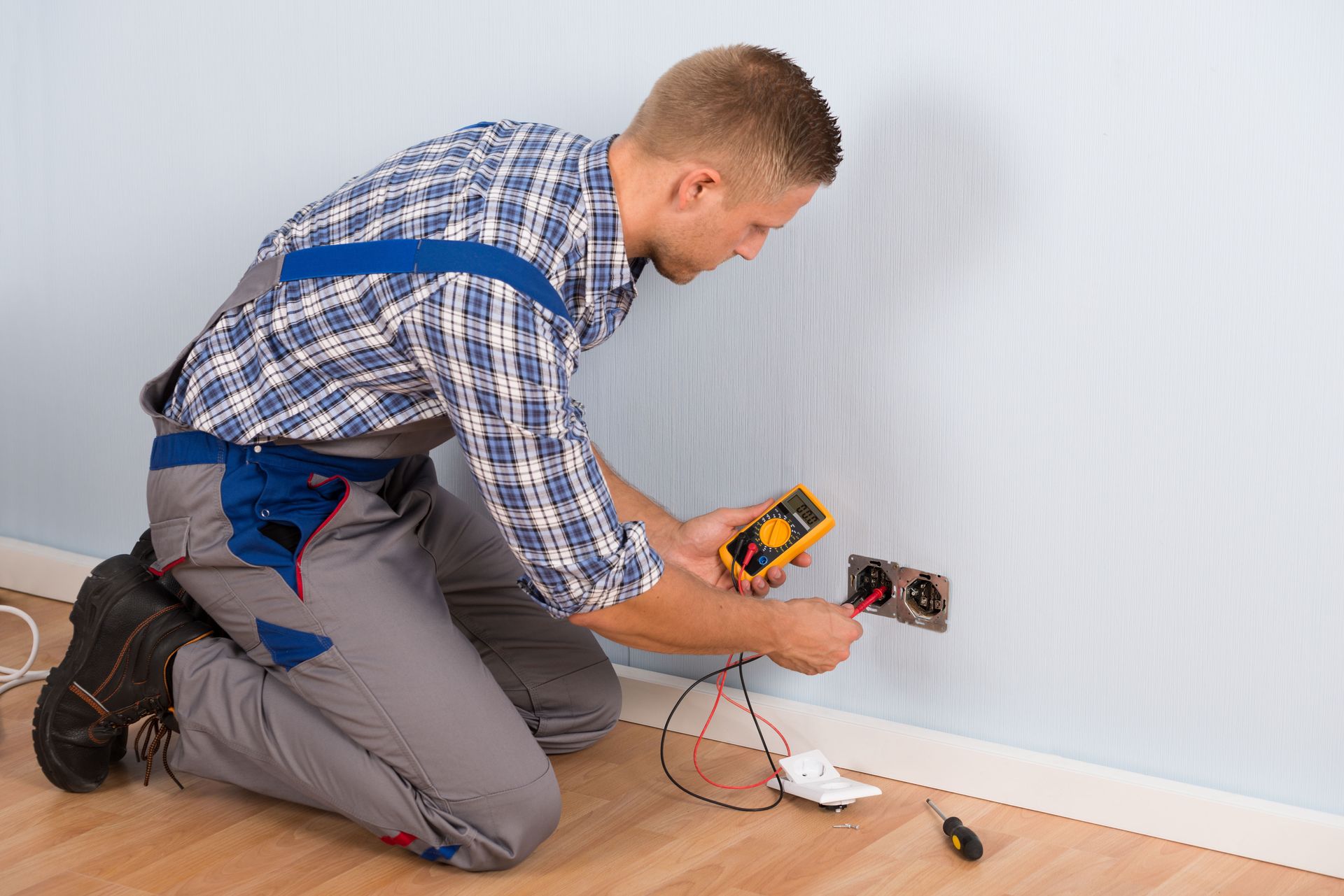 Electrician tests electrical outlet with multimeter.