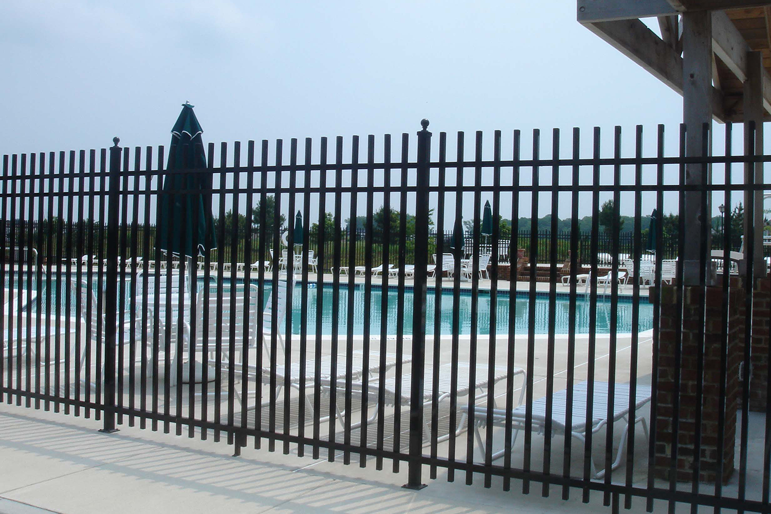 A fence surrounds a swimming pool with chairs and umbrellas.