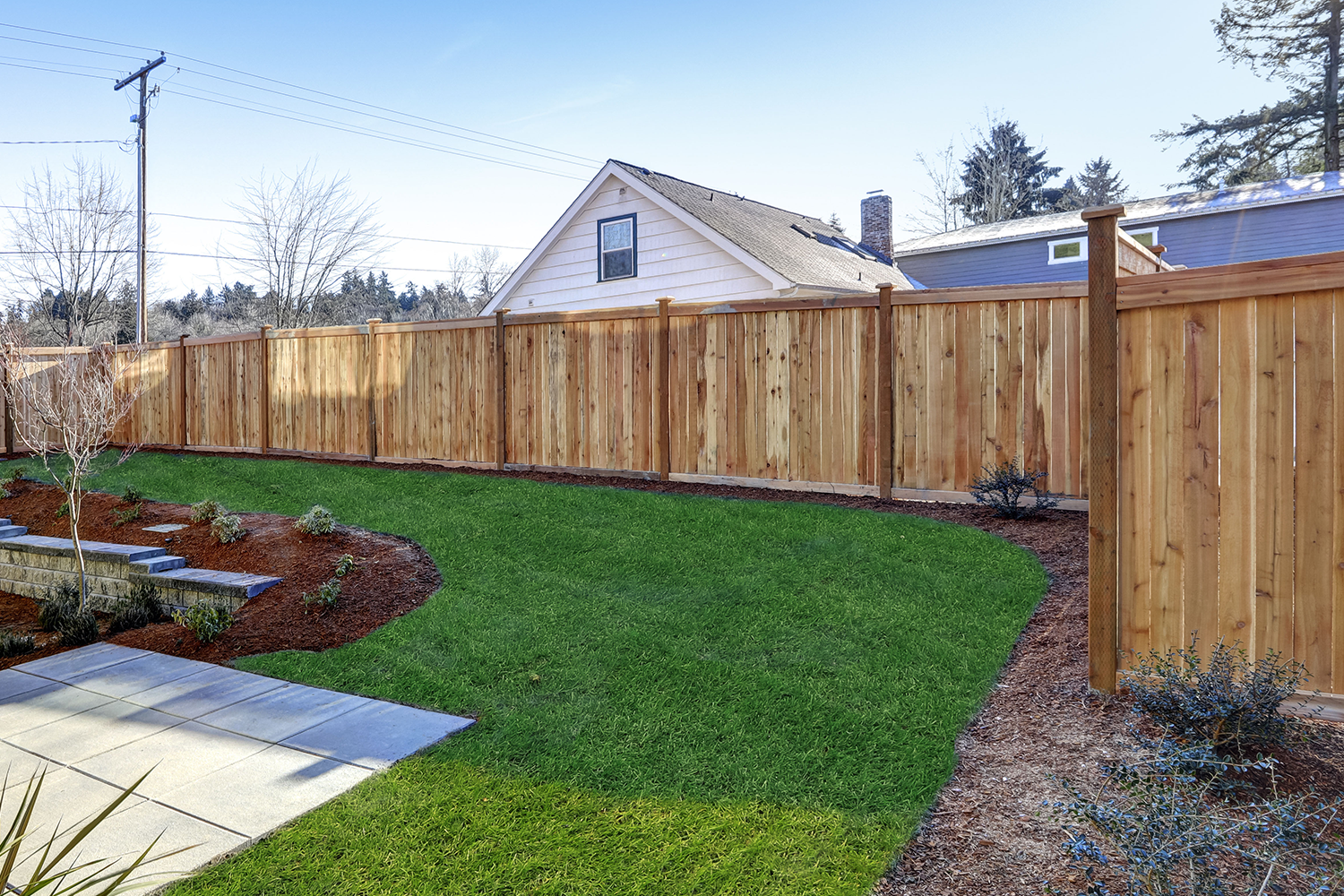 A wooden fence surrounds a lush green lawn in a backyard.