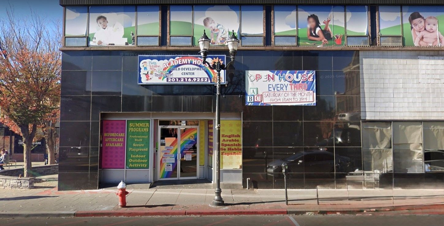 Storefront of a childcare center with black facade, rainbow signage, and window displays featuring children.