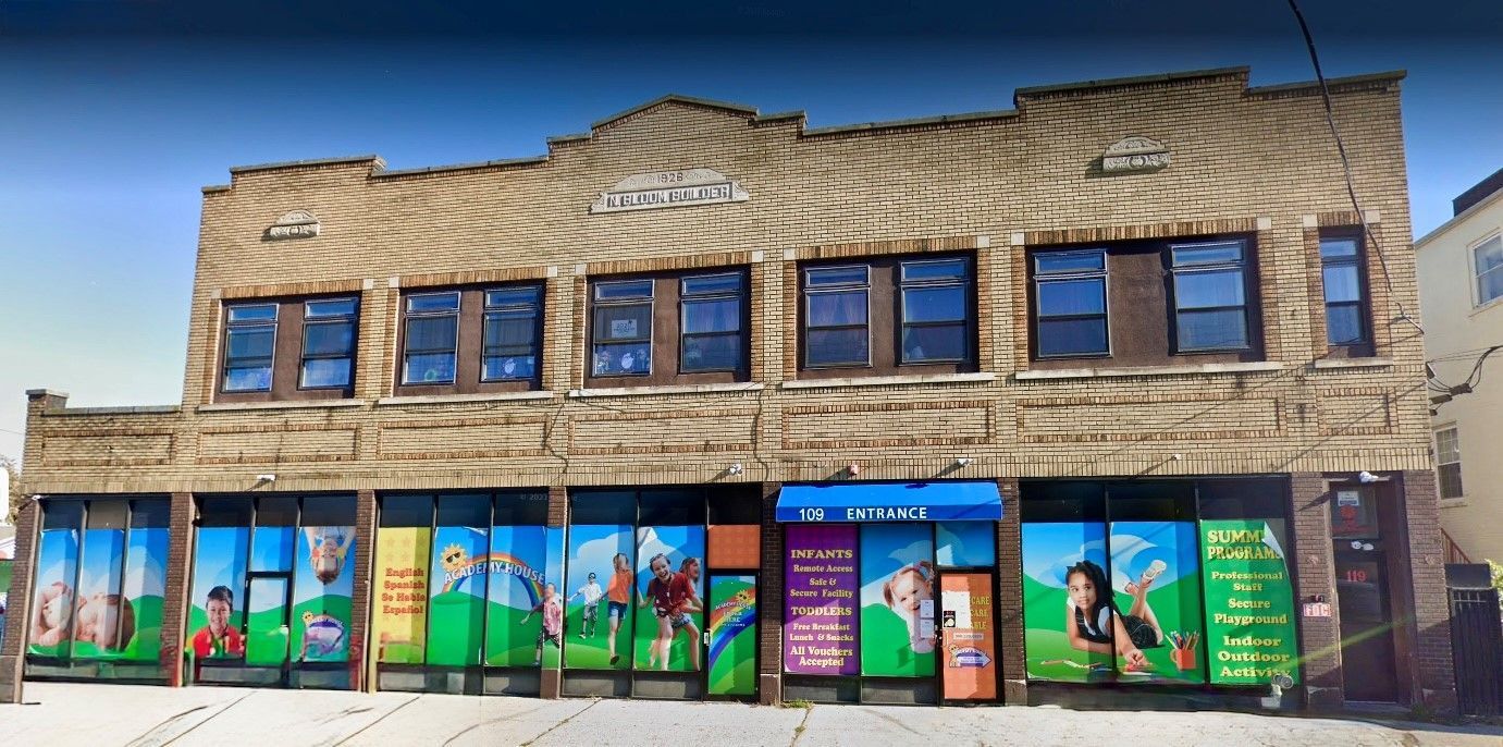 A two-story tan brick building with ground-floor storefront windows featuring colorful graphics of children playing.